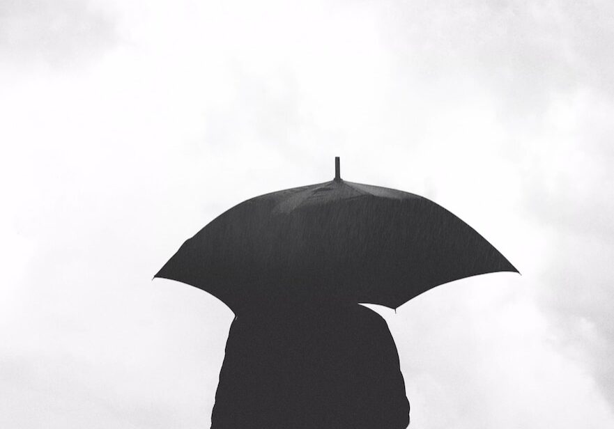 silhouette of person under umbrella under cloudy sky